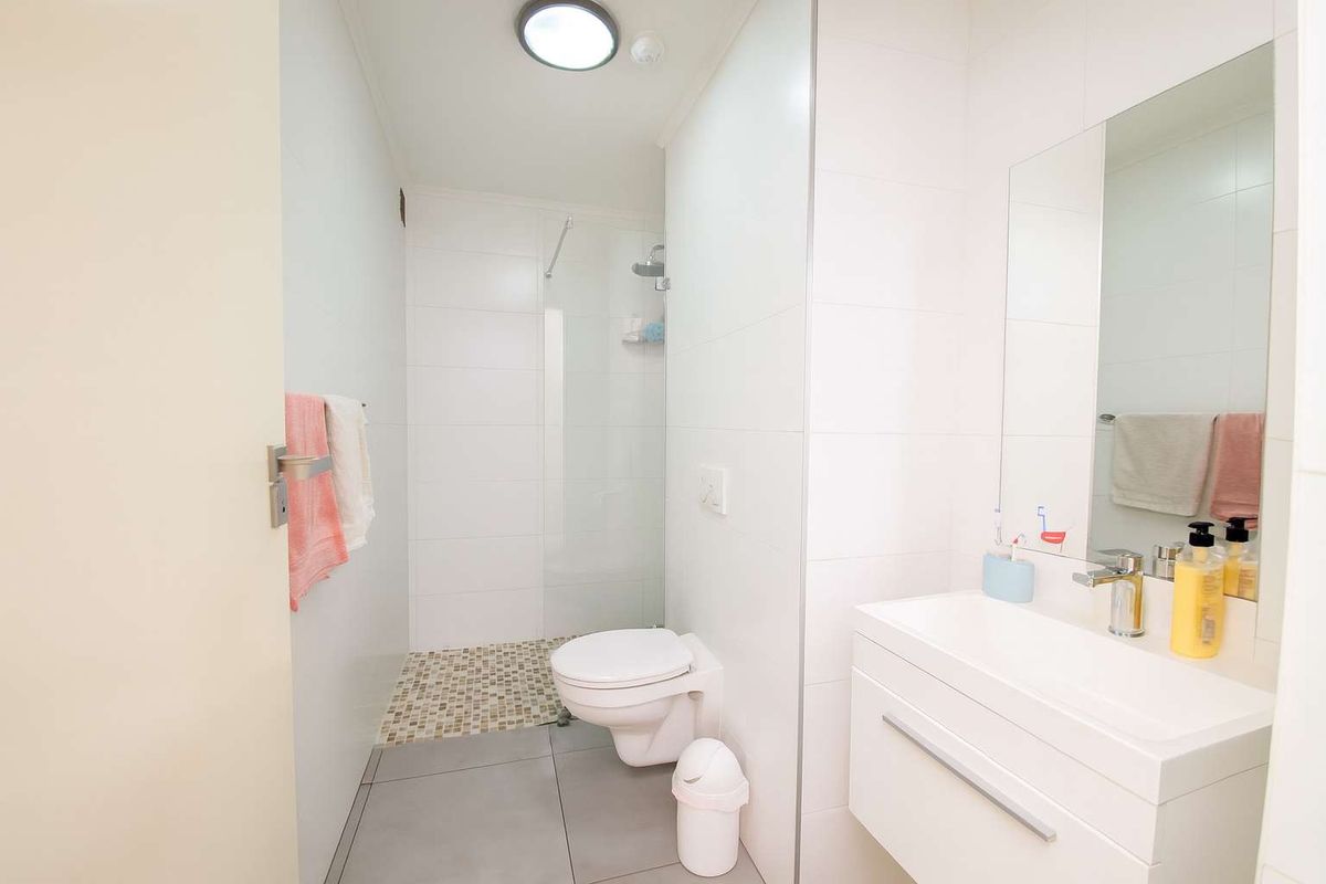 A clean, modern bathroom featuring a wall-mounted vanity, a walk-in shower with a glass screen, and neutral floor and wall tiling.