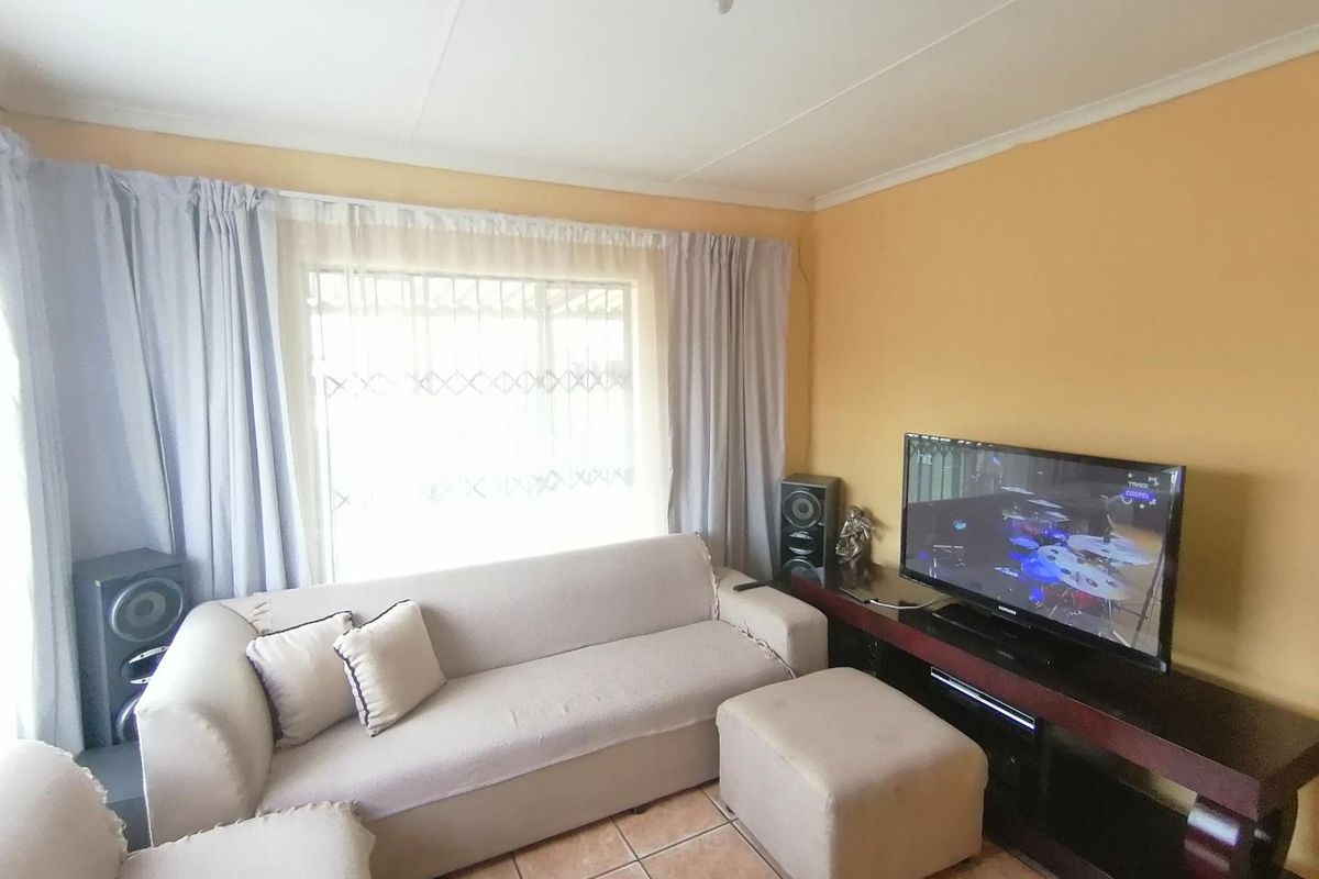 A living room featuring tiled flooring, a large window with security bars, and neutral wall finishes.