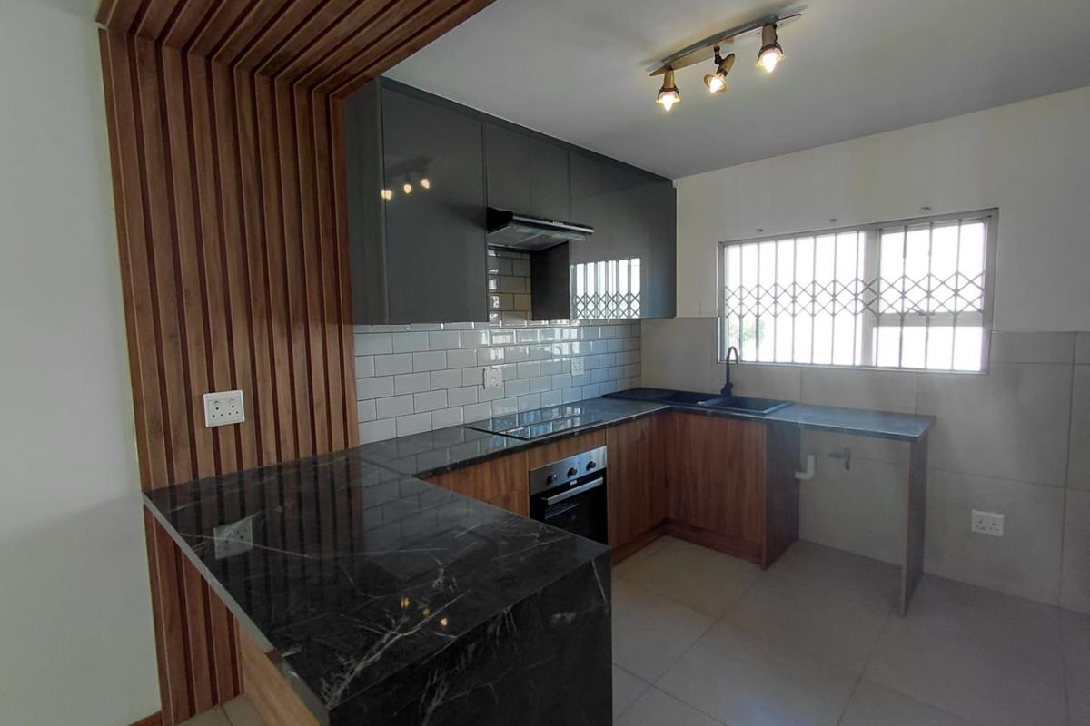 Modern kitchen featuring dark cabinetry, stone countertops, subway tile backsplash, integrated oven, and a stylish slatted wood accent wall.