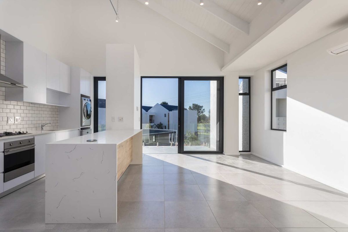 Modern open-plan kitchen and living area featuring a stone-topped island, built-in appliances, vaulted ceilings, and large sliding doors leading to an outdoor space.
