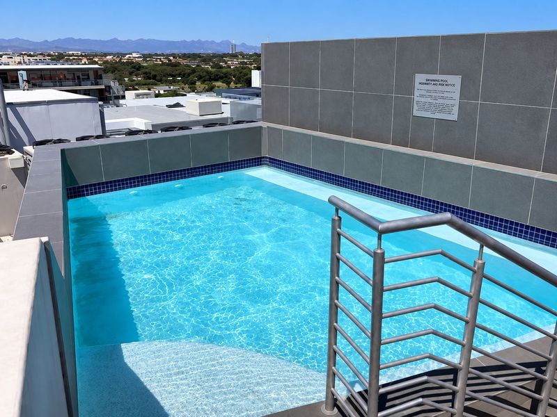 A modern rooftop swimming pool featuring tiled finishes, a stainless steel handrail, and panoramic views of the surrounding landscape.