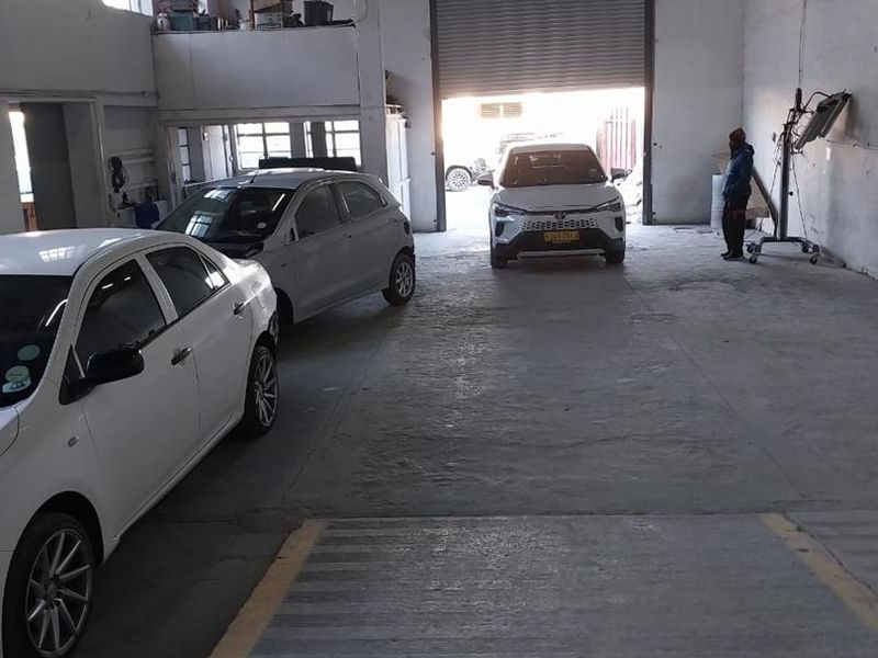 Spacious industrial garage featuring high ceilings with exposed timber trusses, a large roller shutter door, and a mezzanine level for additional storage.