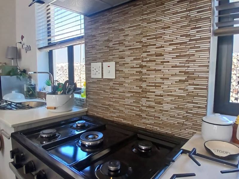 A functional kitchen area featuring a gas stove, extractor fan, and a decorative tiled backsplash with integrated sink and countertop space.