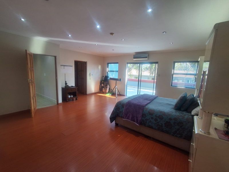 Spacious bedroom featuring laminate flooring, recessed downlighting, a split-system air conditioner, and sliding glass doors leading to an outdoor balcony area.