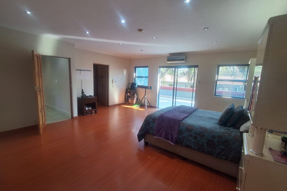 Spacious bedroom featuring laminate flooring, recessed downlighting, a split-system air conditioner, and sliding glass doors leading to an outdoor balcony area.