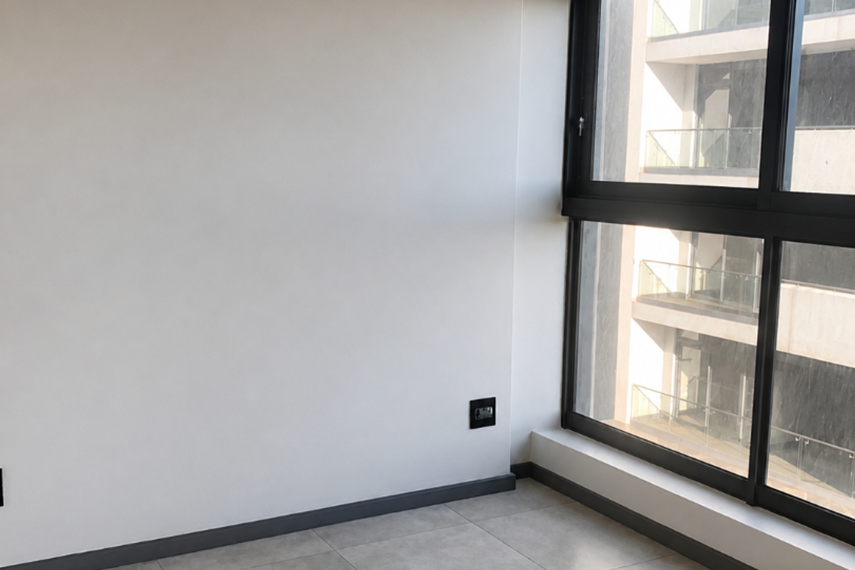 A bright, empty bedroom featuring modern large-format floor tiles, neutral walls, and a large window with dark framing.