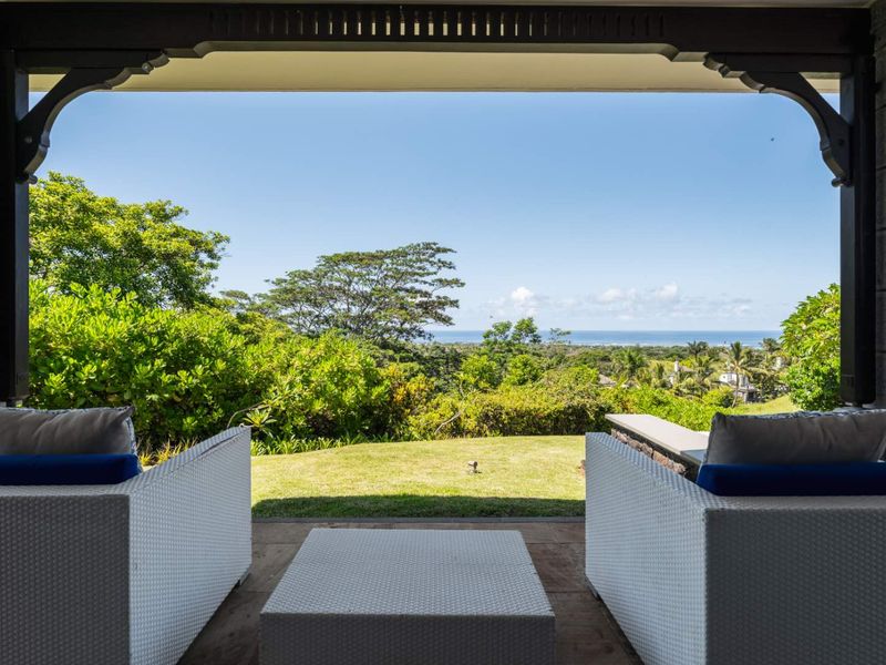 A covered patio area offering expansive views of the lush garden and distant ocean horizon.