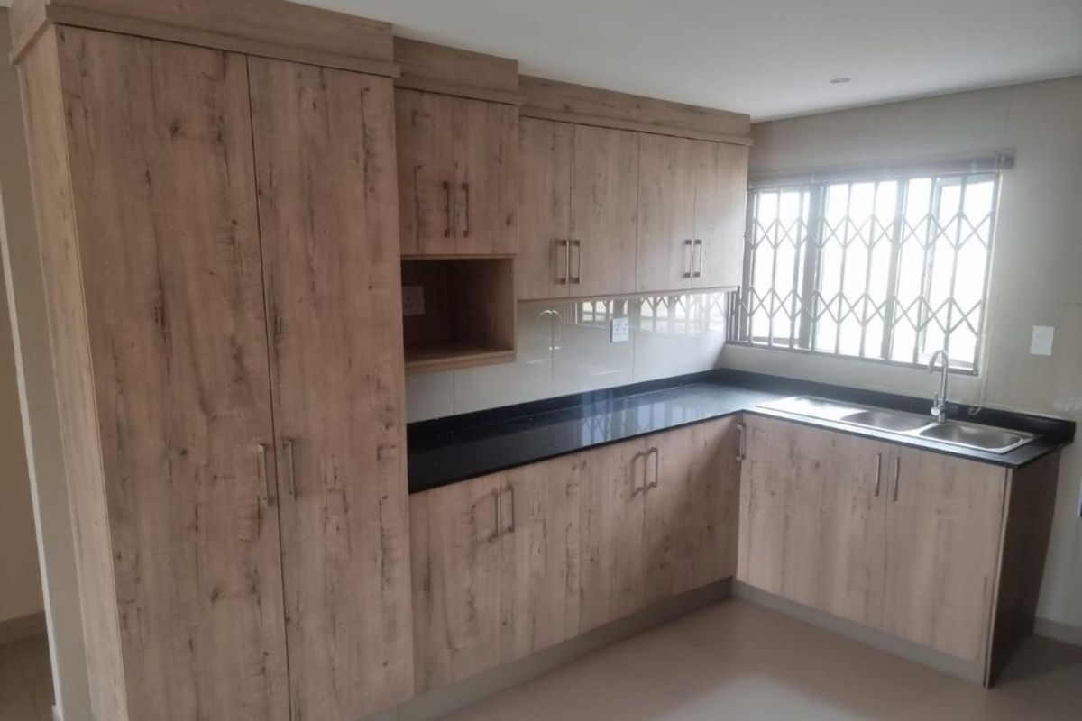 Modern kitchen featuring wood-look laminate cabinetry, black granite countertops, and a stainless steel double sink with a security gate on the window.