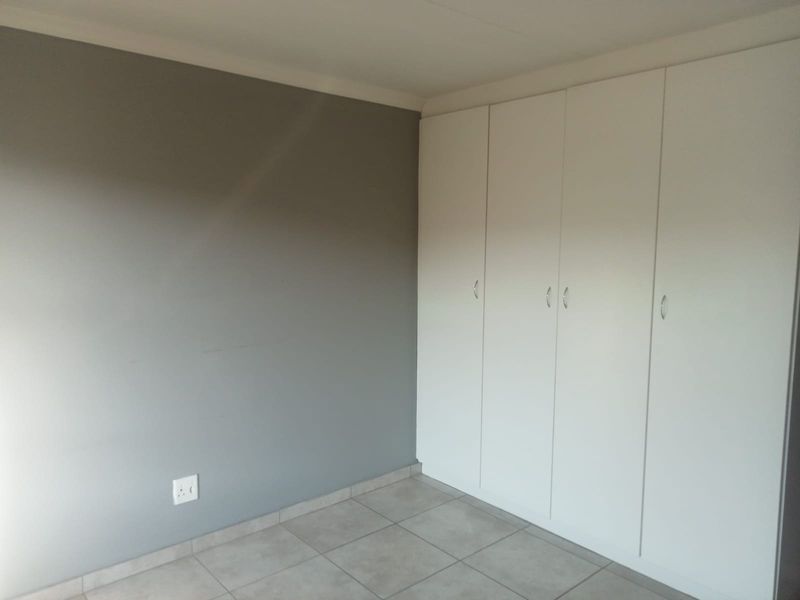 A clean, empty bedroom featuring neutral grey walls, tiled flooring, and ample built-in cupboard storage.