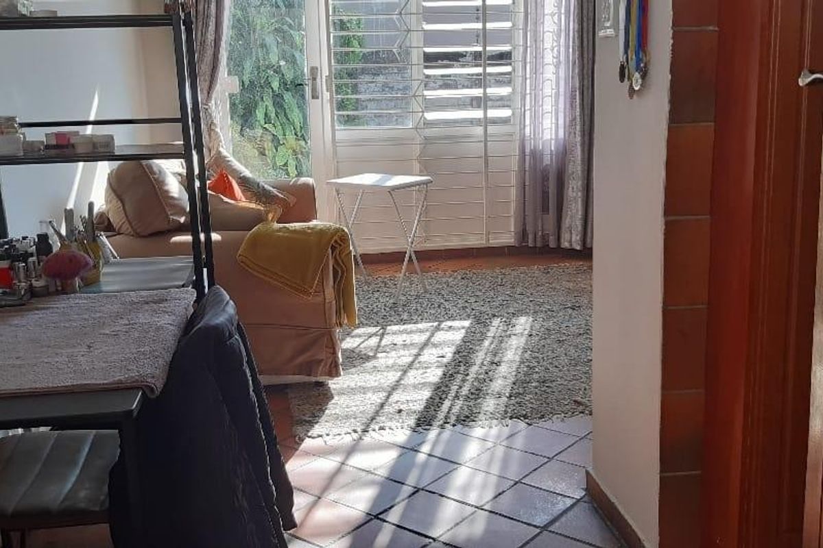 A living area featuring tiled flooring and a sliding glass door with security gate, providing access to the exterior.