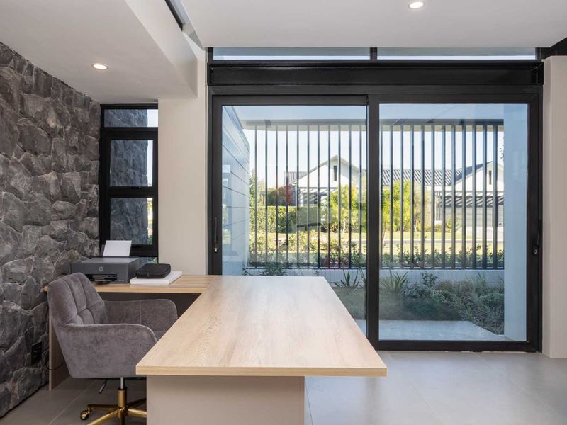 Modern home office featuring a striking stone feature wall, large sliding glass doors providing natural light, and sleek tiled flooring.