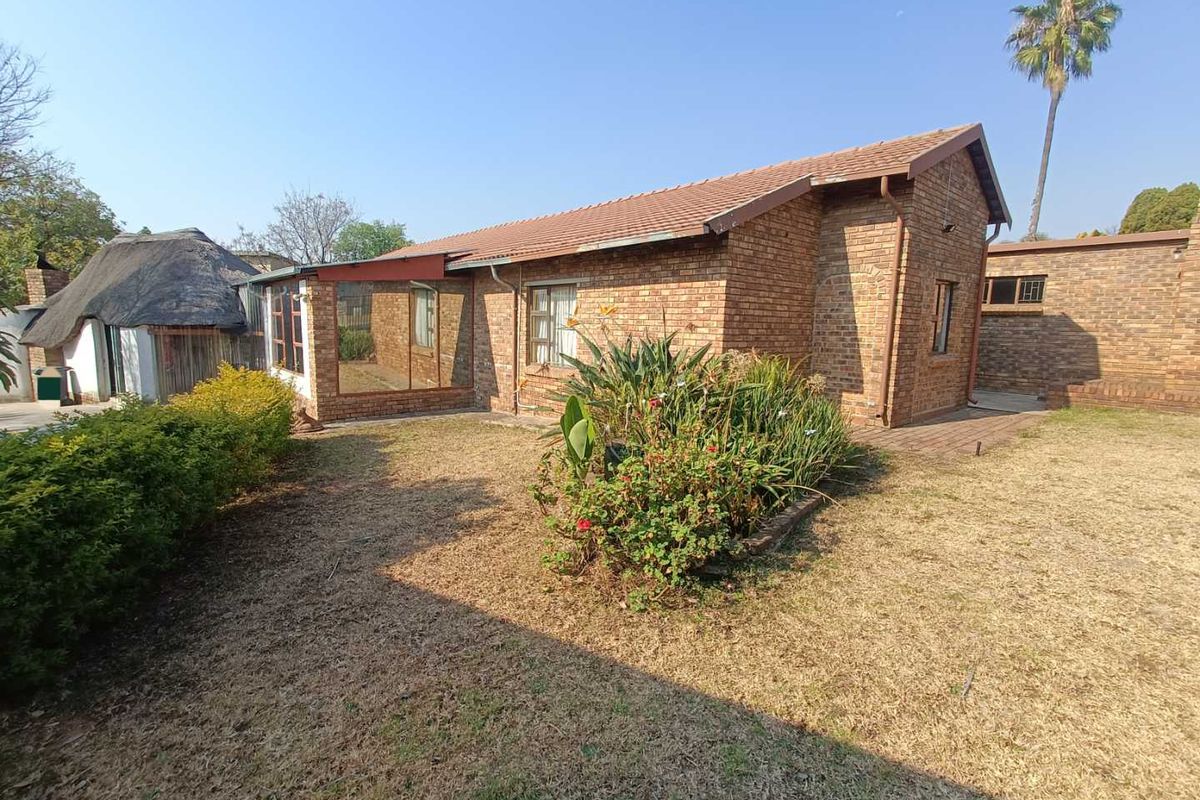 Rear view of a face brick house featuring a tiled roof, an enclosed patio area, and a surrounding garden with a paved walkway.