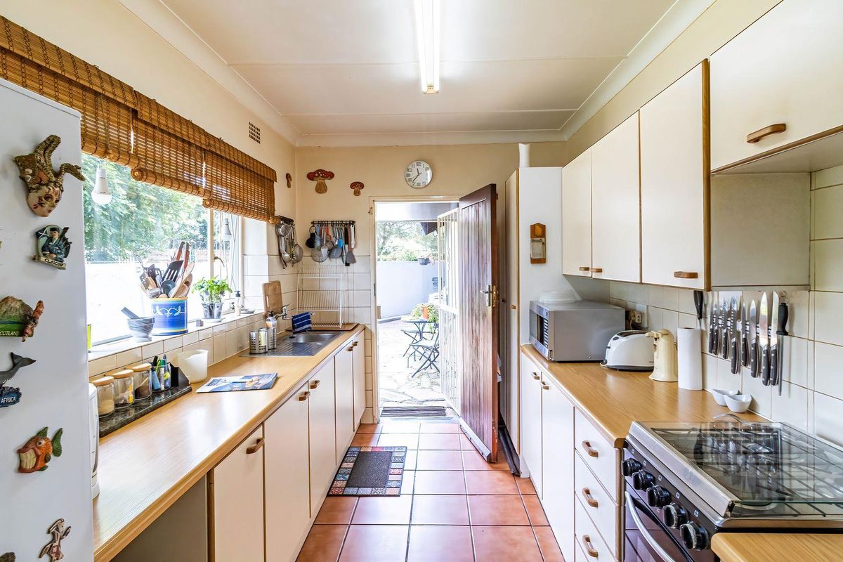 A functional galley-style kitchen featuring laminate countertops, tiled backsplash, built-in oven and hob, and direct access to the rear outdoor area.