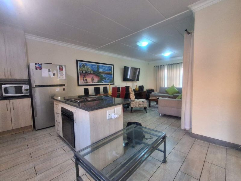 Open-plan living area featuring a kitchen with a central island, granite countertops, built-in oven, and tiled flooring throughout the combined kitchen and lounge space.