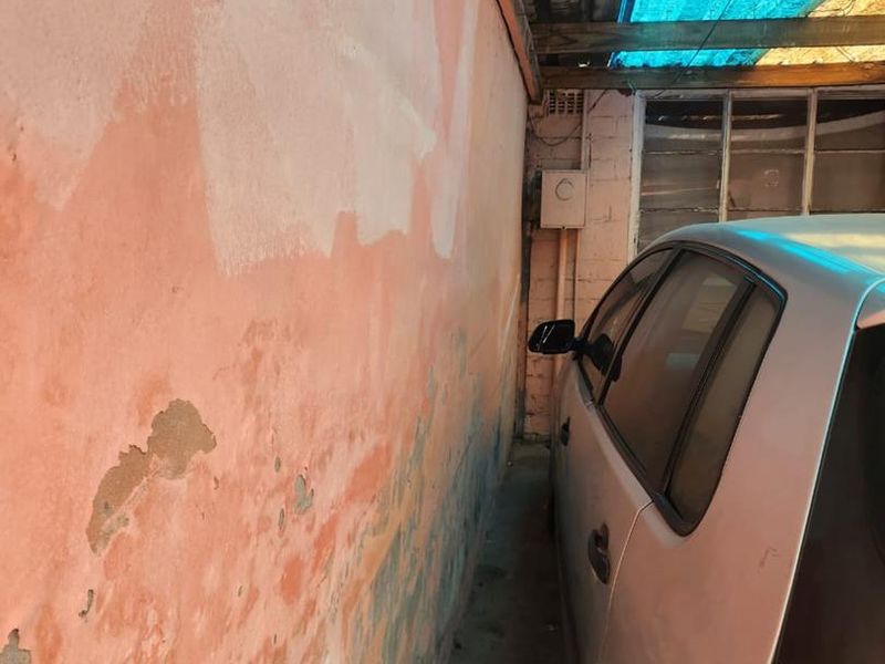 A narrow garage space featuring exposed timber rafters and a masonry wall showing significant signs of plaster degradation and peeling paint.