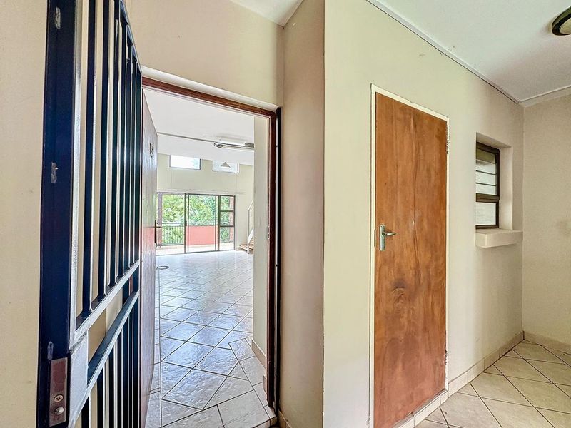Entrance area featuring tiled flooring, a security gate, and a wooden door leading into an open-plan living space.