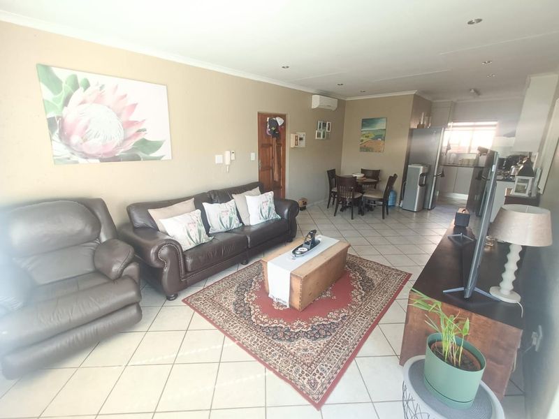Spacious open-plan living and dining area featuring tiled flooring, recessed lighting, and a wall-mounted air conditioning unit, flowing into the kitchen space.
