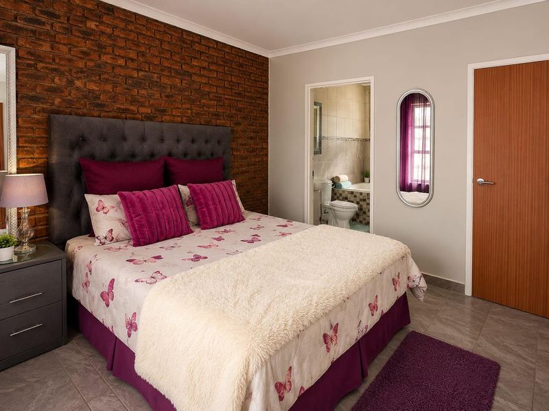 A well-maintained bedroom featuring an exposed brick accent wall, tiled flooring, and direct access to an en-suite bathroom.