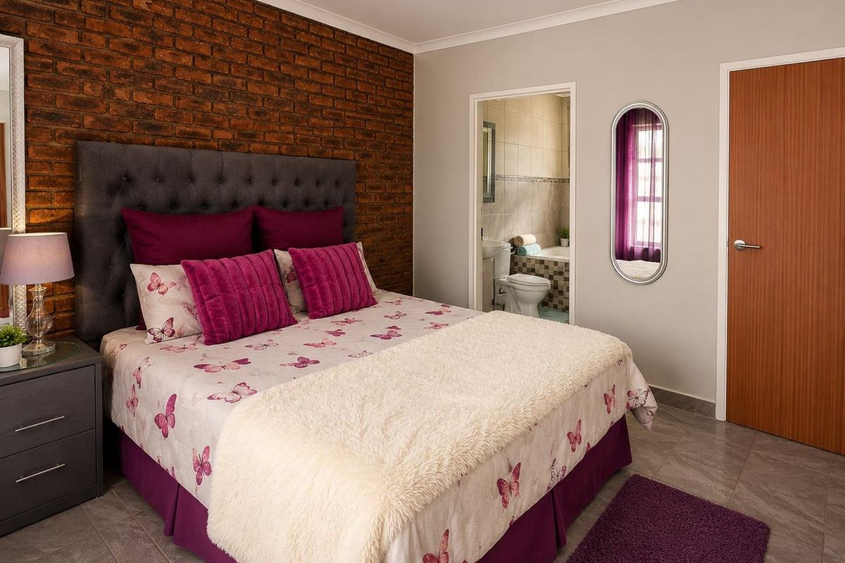 A well-maintained bedroom featuring an exposed brick accent wall, tiled flooring, and direct access to an en-suite bathroom.