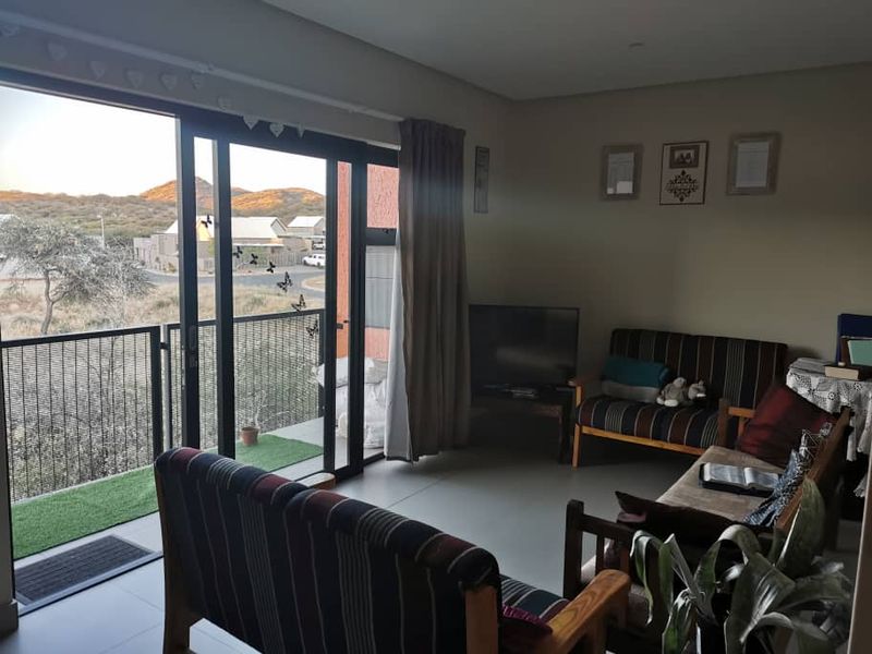 A living room featuring tiled floors and a large sliding glass door that opens onto a balcony with scenic views.