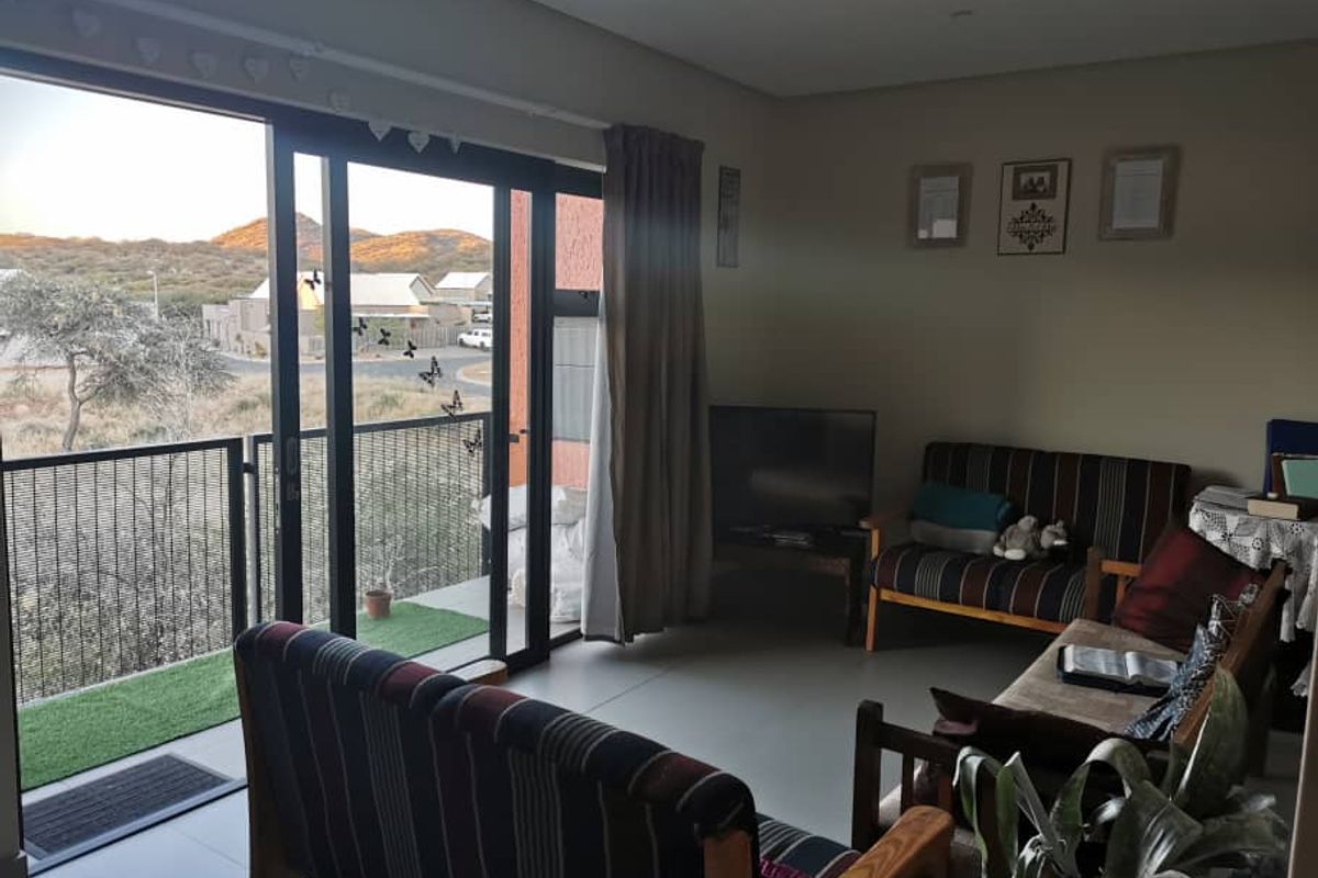 A living room featuring tiled floors and a large sliding glass door that opens onto a balcony with scenic views.