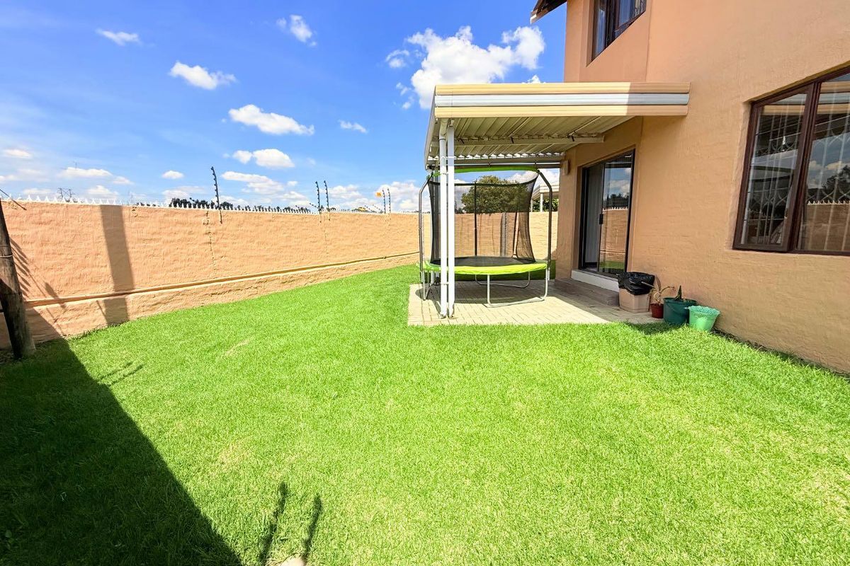 A private rear garden featuring a paved patio area with a covered pergola, well-maintained lawn, and perimeter wall with electric fencing.