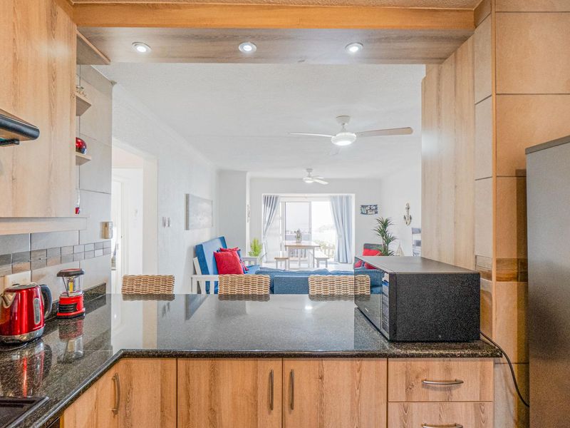 Open-plan kitchen featuring granite countertops and wood-look cabinetry, flowing into a bright living area with ceiling fans and access to a balcony.