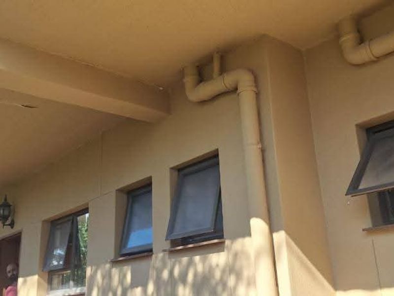 Exterior view of the building rear featuring multiple awning windows, external plumbing pipes, and a covered overhang area with visible plaster damage.