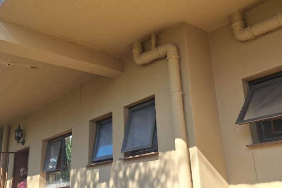Exterior view of the building rear featuring multiple awning windows, external plumbing pipes, and a covered overhang area with visible plaster damage.