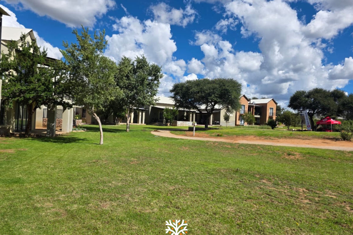 A view of the communal garden area and townhouse complex exterior, featuring well-maintained lawns and mature trees.
