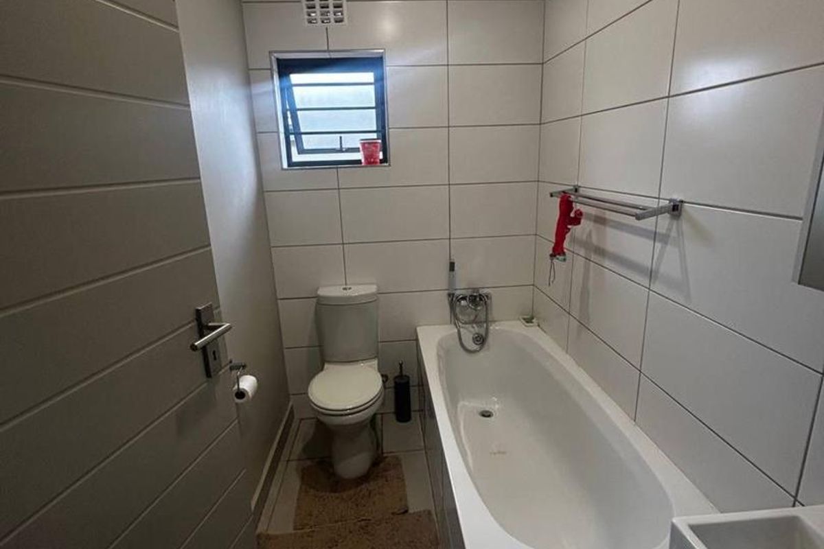A compact bathroom featuring full-height wall tiling, a built-in bathtub with shower mixer, a standard toilet, and a wall-mounted basin.