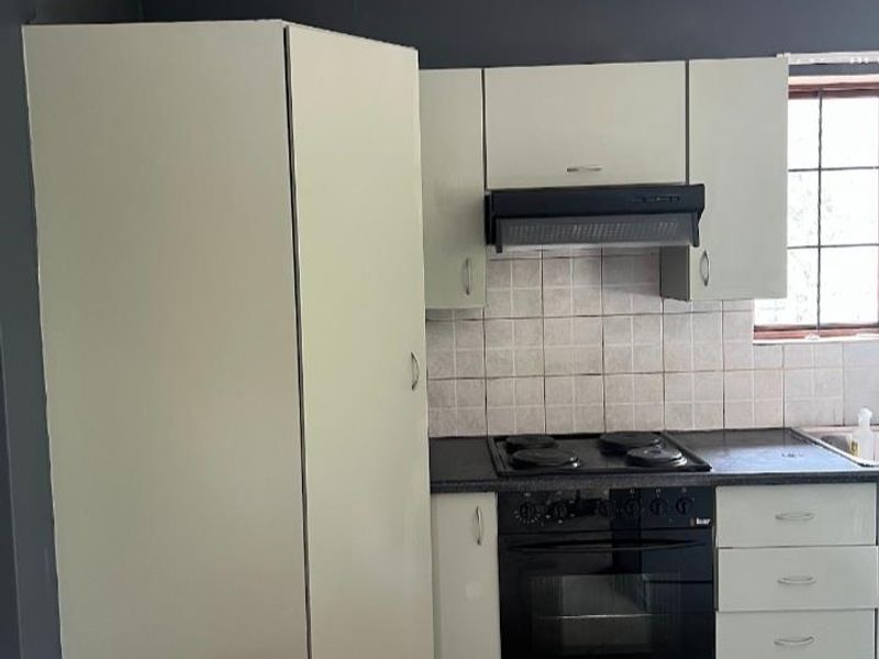 A functional kitchen featuring built-in cabinetry, an integrated oven and hob, extractor fan, and tiled backsplash with neutral floor tiles.