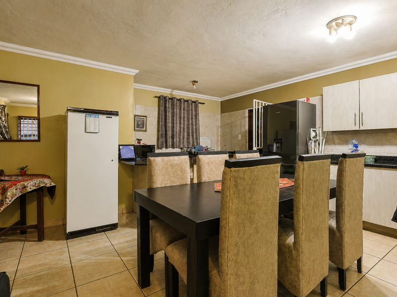 Open plan kitchen and dining area featuring tiled flooring, built-in cabinetry with granite countertops, and a neutral color palette.