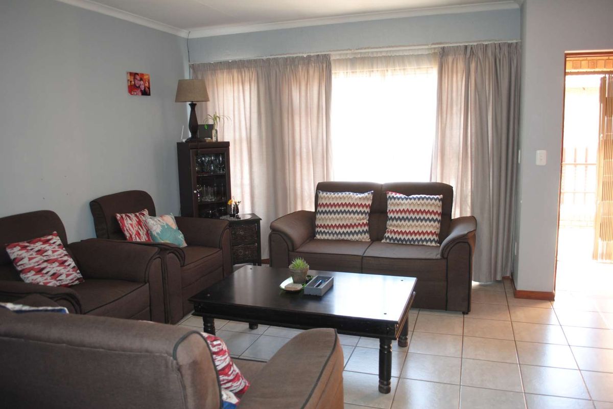 A comfortable living room featuring tiled flooring and large windows with curtains, providing natural light and access to an adjacent area.