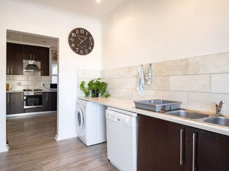 A functional laundry area featuring built-in cabinetry, a double stainless steel sink, and modern tiled splashbacks, with an adjacent view into the kitchen.