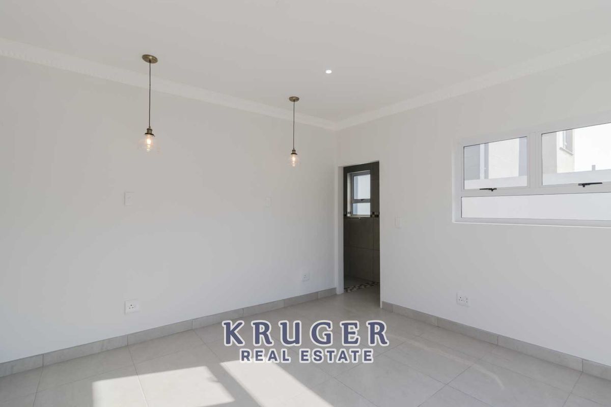 A bright, neutral-toned living area featuring tiled flooring, modern pendant lighting, and a doorway leading to an adjacent space.