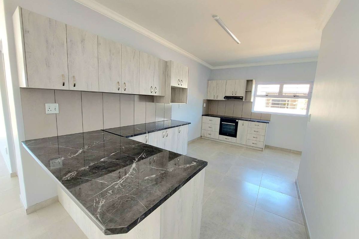 Modern kitchen featuring light wood-grain cabinetry, dark marble-effect countertops, built-in oven, and extractor fan with tiled flooring.