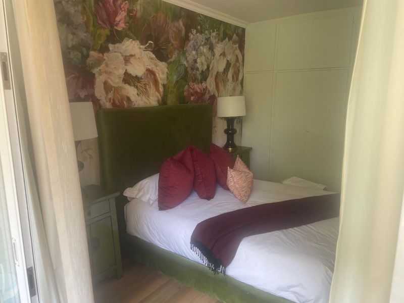 A cozy bedroom featuring built-in cupboards and hardwood flooring, accented by a floral feature wall.
