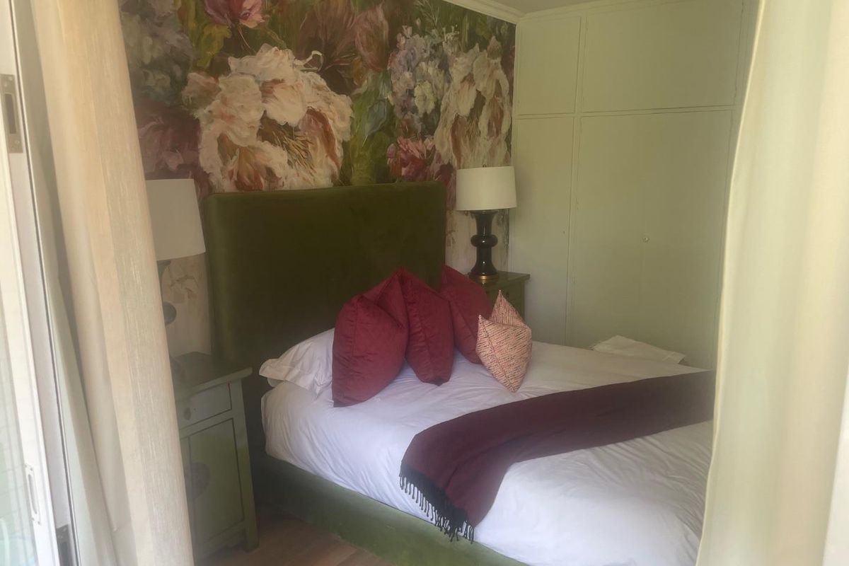 A cozy bedroom featuring built-in cupboards and hardwood flooring, accented by a floral feature wall.