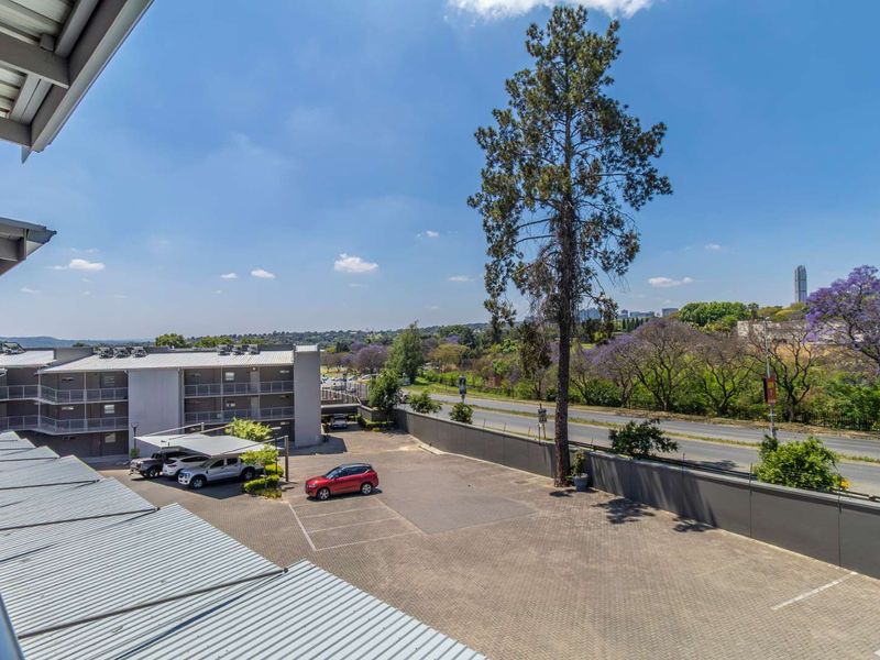 Elevated view overlooking a paved parking area, perimeter wall, and surrounding landscape with distant city skyline.