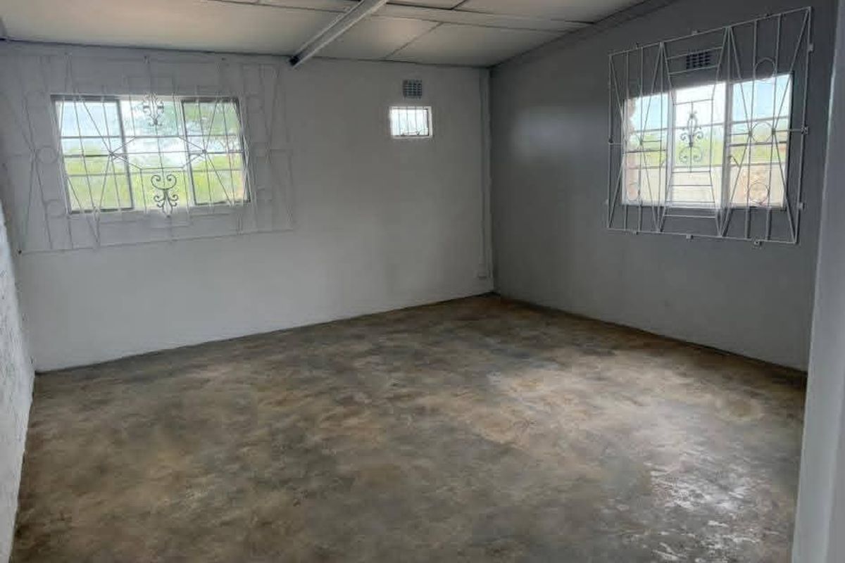 An empty bedroom featuring concrete flooring, security bars on the windows, and basic lighting, offering a blank canvas for renovation.