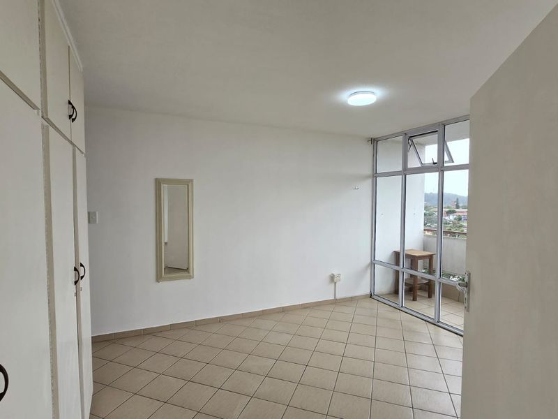 An empty bedroom featuring built-in cupboards, tiled flooring, and a large glass window wall providing natural light and access to a balcony.