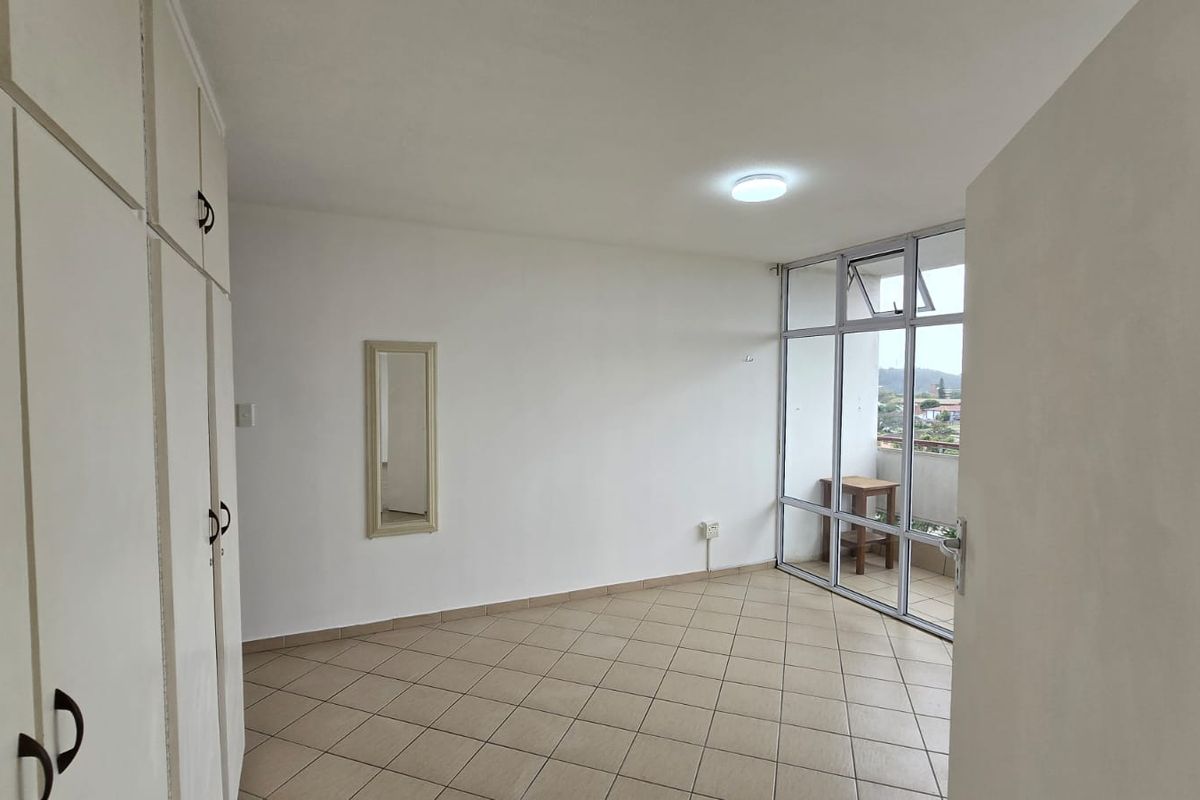 An empty bedroom featuring built-in cupboards, tiled flooring, and a large glass window wall providing natural light and access to a balcony.