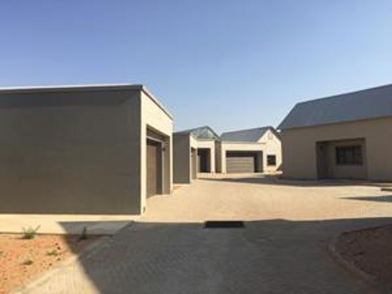 A view of the townhouse complex driveway featuring multiple garage entrances and modern plastered exterior facades.