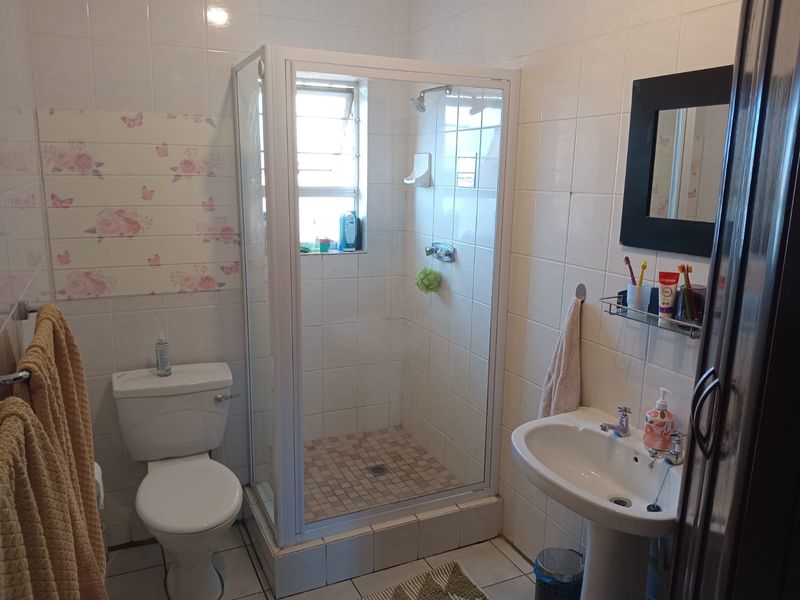 A functional bathroom featuring a shower enclosure, pedestal basin, and toilet with neutral wall and floor tiling.