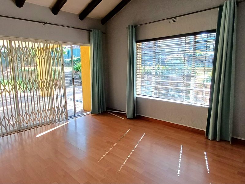 Spacious living room featuring exposed timber ceiling beams, laminate flooring, and large windows with access to an outdoor patio area.