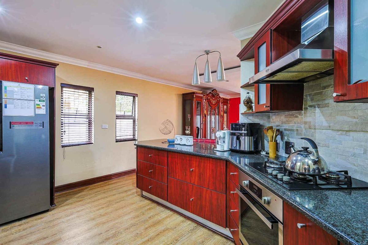 A functional kitchen featuring dark wood cabinetry, granite countertops, a built-in gas hob, an extractor fan, and a tiled backsplash.
