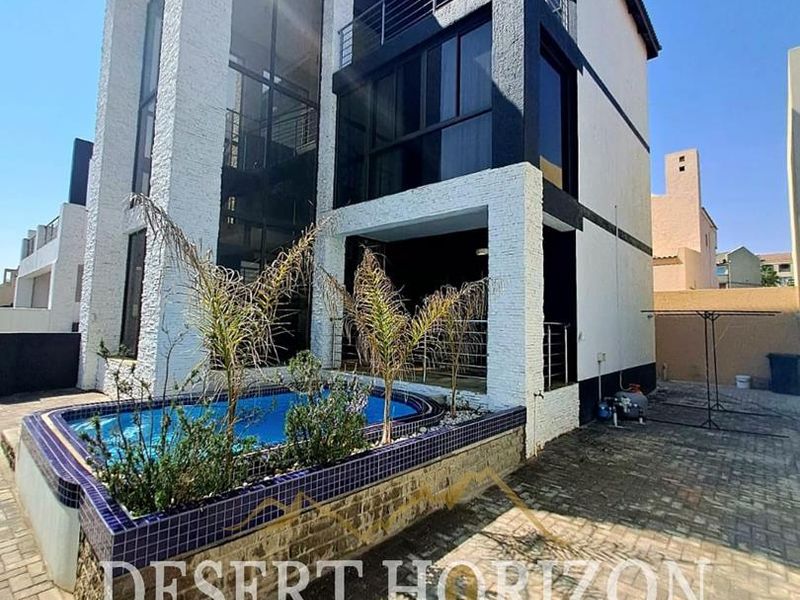 Rear exterior view of a multi-level house featuring a private swimming pool, paved patio area, and upper-level balconies with metal railings.