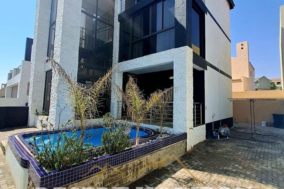 Rear exterior view of a multi-level house featuring a private swimming pool, paved patio area, and upper-level balconies with metal railings.