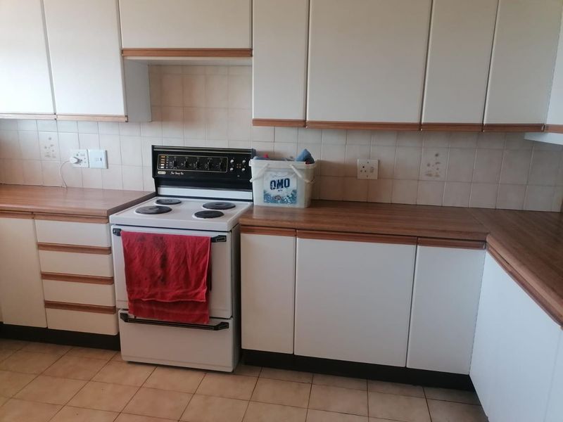 A functional kitchen featuring white cabinetry with wood trim, laminate countertops, a tiled backsplash, and a freestanding stove.